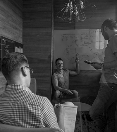 Black-and-white photo of three men strategizing around a dry erase board, symbolizing collaborative marketing engagement where clients manage their strengths and WeKinnect Global assists in Texas.
